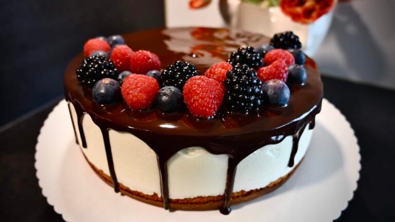 Eine himmlische Vogelmilch-Torte mit Schokoladenglasur, frischen Himbeeren, Brombeeren und Heidelbeeren, gefüllt mit einer zarten Schicht Soufflé.