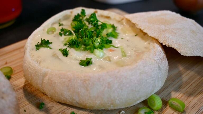 Ein warmes, knuspriges Brotlaib, gefüllt mit cremiger Kartoffelsuppe und bestreut mit frischen Kräutern, für ein rustikales Esserlebnis.