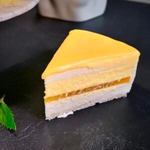 Ein Stück Mango-Maracuja-Torte steht auf einer schwarzen Schieferplatte.