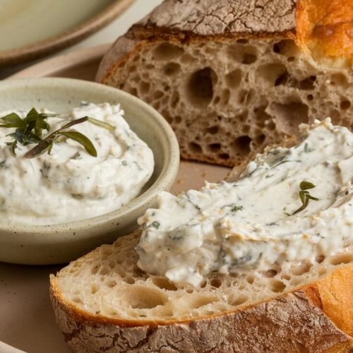 Frisches Sauerteigbrot mit knuspriger Kruste, bestrichen mit cremigem Weißfisch-Dip, serviert auf einem rustikalen Teller.