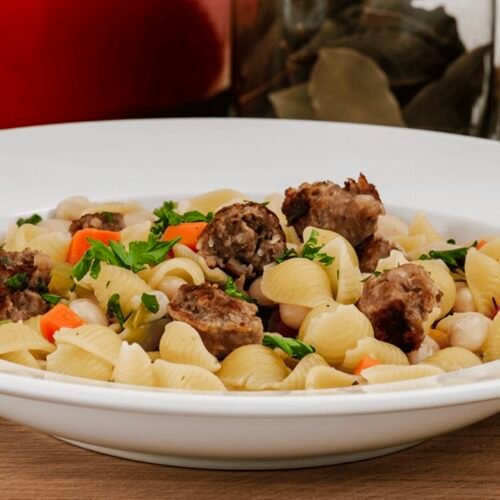 Zarte Schweinefiletstreifen in einer cremigen Tomaten-Bohnen-Soße mit Pasta und frischem Rucola, angerichtet auf einem Teller.