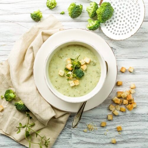 Eine cremige Brokkolisuppe, serviert mit knusprigen Croutons und frischen Kräutern auf einem rustikalen Holztisch.